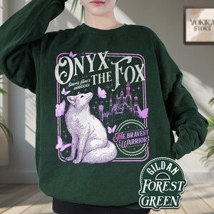 Może przedstawiać: Leśnozielona bluza z nadrukiem białego lisa, motyli i zamku, z napisem "ONYX THE FOX" i "THE BRAVEST WARRIOR". Bluza wykonana jest z materiału Gildan Forest Green.