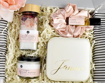 Könnte beinhalten: Eine Geschenkbox gefüllt mit Selbstpflegeartikeln, darunter Badesalz, Körperbutter, ätherisches Öl und ein Haargummi. Die Box ist mit einem personalisierten Namensschild verziert, auf dem "Janine" steht.