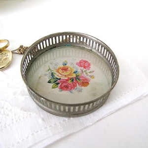 May include: A silver metal trinket tray with a floral design on the bottom. The tray has a decorative, openwork rim.
