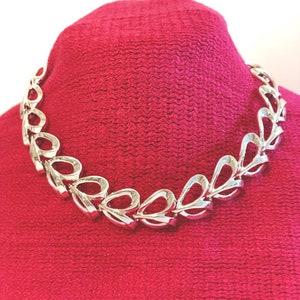 May include: A silver necklace with a chain made of linked, open, teardrop-shaped pieces.