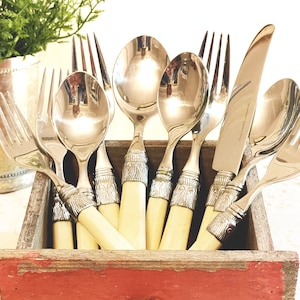 May include: A collection of vintage silverware, including forks, spoons, and knives, with cream-colored handles and ornate silver detailing. The utensils are arranged in a rustic, red-painted wooden drawer, suggesting a farmhouse aesthetic.