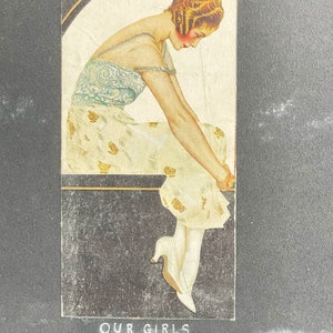 May include: A vintage postcard featuring a woman in a white dress with gold accents, sitting on a ledge. The text on the postcard reads "Often they think of us Our girls at home".