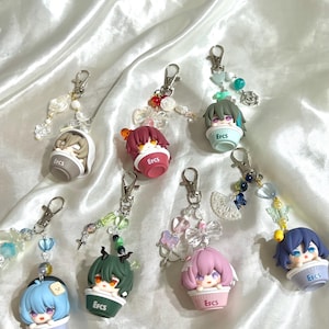 May include: A collection of seven keychains featuring anime-style characters in small cup-like containers. Each keychain has a different character with unique hair color and accessories. The containers have the text "EFCS" printed on them.