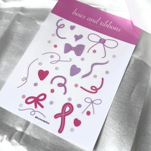 Puede incluir: Una hoja de pegatinas con un diseño rosa y morado con lazos, cintas, corazones y puntos. El texto "bows and ribbons" está en la parte superior. La hoja de pegatinas está sobre un fondo blanco.