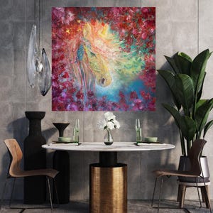 May include: A colourful square canvas painting of a horse's head, surrounded by flowers. The horse is in yellow, white, and blue, with a flowing mane. The flowers are red, pink, and purple. The artwork is displayed in a modern dining room setting with a marble table.