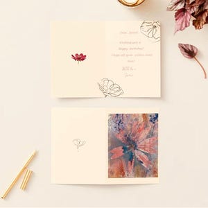 May include: Two cream-colored greeting cards, one open and one closed, with floral illustrations and handwritten text. The open card features a watercolor floral design and the text "Wishing you a happy birthday!" A gold pen rests nearby.