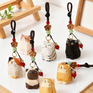 May include: A collection of wooden cat figurines in various colors, including black, white, brown, and orange. Each cat has a smiling face and is attached to a decorative cord with beads and wooden flowers. These cat figurines are ideal for cat lovers.