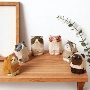 May include: A collection of hand-carved wooden cat figurines in various colors and patterns, including orange, gray, brown, and white. The cats are displayed on a wooden shelf, showcasing their unique designs and expressions.
