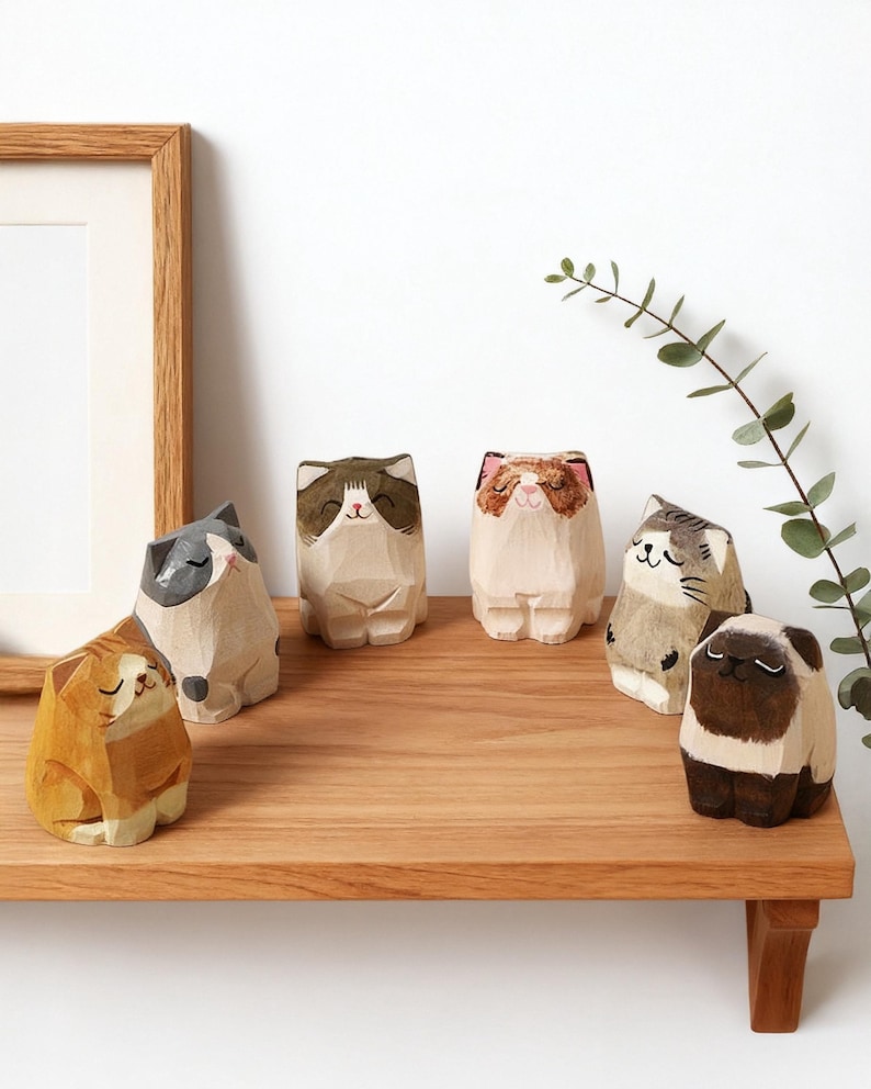 May include: A collection of hand-carved wooden cat figurines in various colors and patterns, including orange, gray, brown, and white. The cats are displayed on a wooden shelf, showcasing their unique designs and expressions.