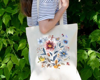 Peut inclure: Sac fourre-tout crème avec un motif floral. Le motif présente une grande fleur bordeaux au centre, entourée de fleurs bleues, blanches et rouges, de feuilles vertes et de petits oiseaux. Le sac est tenu devant un fond de feuillage vert.