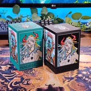 Könnte beinhalten: Zwei quadratische Kartenaufbewahrungsboxen. Eine ist türkis, die andere schwarz. Beide zeigen eine detaillierte Illustration im Anime-Stil einer Frau mit weißen Haaren, roten Hörnern und einem Kimono. Die Boxen haben ein passendes Design auf der Oberseite und den Seiten.