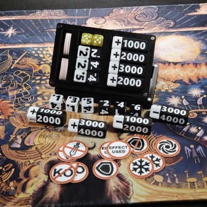 Könnte beinhalten: Ein schwarzer Spiel-Score-Tracker mit weißen Zahlen und Würfeln. Enthält Würfel, Spielsteine und einen Score-Keeper mit Zahlen wie 1000, 2000, 3000 und 4000. Die Spielsteine befinden sich auf einer gemusterten Oberfläche.