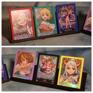 Könnte beinhalten: Ein schwarzer Präsentationsständer mit sechs farbenfrohen Sammelkarten. Jede Karte zeigt einen anderen Anime-Charakter mit lebendigen Kunstwerken und Text. Die Karten haben glitzernde Ränder in Rot, Grün, Blau, Lila, Schwarz und Gelb. Die Charaktere sind Uta, Carrot, Boa Hancock, Charlotte Pudding, Koala und Yamato.