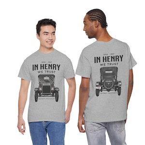 May include: Two people wearing light gray t-shirts with a vintage car graphic. The front of the shirt features a black and white illustration of a classic car with the text "IN HENRY WE TRUST" and "DETROIT MICHIGAN". The back of the shirt has the same text and car graphic.