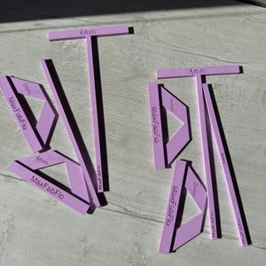 Könnte beinhalten: Ein Set aus hellvioletten Kunststoff-Nähwerkzeugen mit der Aufschrift MaxFabFlo, bestehend aus T-förmigen Führungen mit 6mm-Markierung und dreieckigen Eckschablonen mit 2mm, 4mm und 5mm-Markierung. Die Präzisionswerkzeuge haben eingravierte Maße in Millimetern.