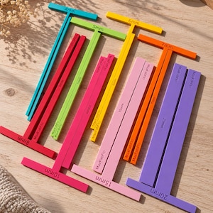 Könnte beinhalten: Eine Sammlung von T-förmigen Messwerkzeugen aus Kunststoff in verschiedenen Farben wie Türkis, Limettengrün, Gelb, Orange, Pink, Rot und Lila. Jedes Werkzeug ist mit seiner Breite in Millimetern beschriftet, wie 4mm, 5mm, 6mm, 7mm, 8mm, 10mm, 15mm und 20mm, und trägt den Markennamen MaxFabFlo auf der Oberfläche.