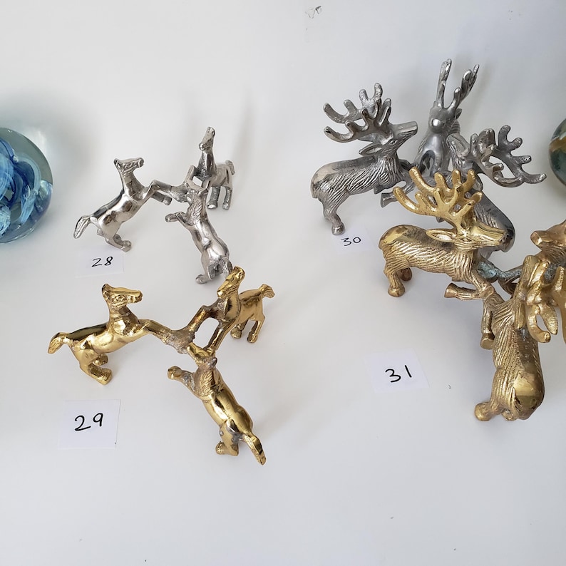 May include: A collection of metallic animal figurines labeled with numbers 28, 29, 30, and 31. The set includes silver-toned horse figures and gold-toned horse figures, alongside silver and gold-toned reindeer figures with detailed antlers.