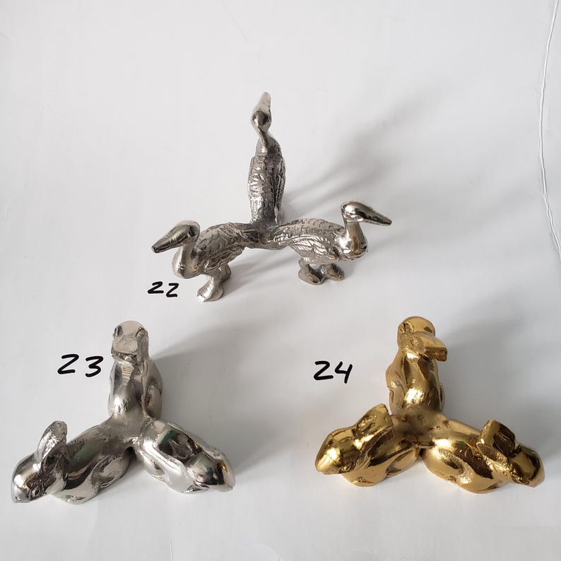 May include: Three metal tripod stands shaped like animals. Item 22 is a silver-toned stand with three bird figures. Item 23 is a silver-toned stand with three rabbit figures. Item 24 is a gold-toned stand with three rabbit figures.