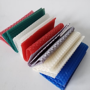 May include: A collection of colorful, textured beeswax sheets in various colors, including red, green, white, and blue. The sheets are arranged in a fan-like display, showcasing their honeycomb pattern. These sheets are likely for candle making or other craft projects.