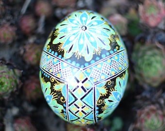 May include: A hand-painted Easter egg with intricate floral and geometric designs in shades of blue, green, yellow, and black.