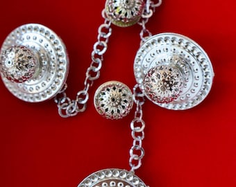 Può includere: Primo piano di una collana e orecchini argentati su uno sfondo rosso vibrante. I gioielli presentano intricati filigrane e piccoli accenti scintillanti. La collana ha un design a catena.