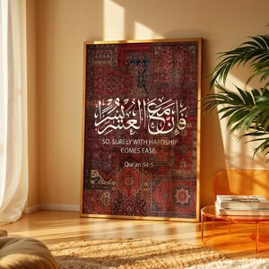 Pu&ograve; includere: Un'opera d'arte incorniciata con un patchwork di motivi di tappeti rossi e bordeaux. Calligrafia araba bianca e testo inglese: "SO, SURELY WITH HARDSHIP COMES EASE. Quran 94:5". L'opera d'arte si trova in una stanza con un'estetica moderna.