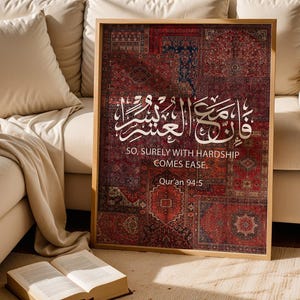 Pu&ograve; includere: Una stampa incorniciata con un motivo a tappeto nei toni del rosso, blu e marrone. Calligrafia araba bianca e testo inglese, "SO, SURELY WITH HARDSHIP COMES EASE. Qur'an 94:5," sono visualizzati. L'opera d'arte &egrave; esposta vicino a un divano beige.
