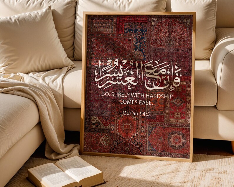 Pu&ograve; includere: Una stampa incorniciata con un motivo a tappeto nei toni del rosso, blu e marrone. Calligrafia araba bianca e testo inglese, "SO, SURELY WITH HARDSHIP COMES EASE. Qur'an 94:5," sono visualizzati. L'opera d'arte &egrave; esposta vicino a un divano beige.