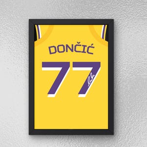 May include: A framed print of a yellow basketball jersey with the name "DONČIĆ" and the number "77" in purple. The jersey has a white outline and a purple signature.