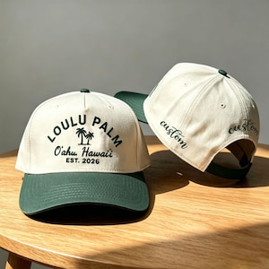 Puede incluir: Dos gorras de béisbol con coronas color crema y viseras verde oscuro. La gorra frontal presenta el texto verde oscuro LOULU PALM, O'ahu, Hawaii, EST. 2026 con un icono de palmera. El lateral de la gorra trasera muestra la palabra custom en cursiva.