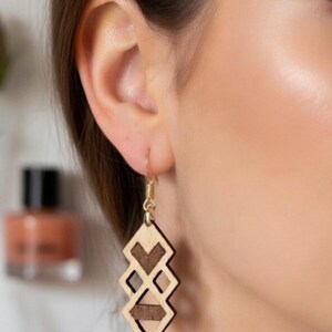 Könnte beinhalten: Geometrische Holzohrringe in hellen und dunklen Holztönen. Die Ohrringe hängen an goldfarbenen Haken. Das Design zeigt Rautenformen und ein Chevron-Muster. Der Markenname "Aurabois" ist sichtbar.