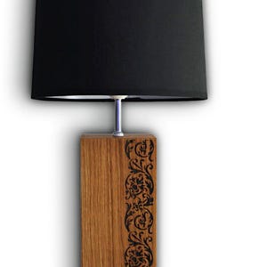 Peut inclure: Un abat-jour noir avec une base en bois. La base est ornée d'un motif floral gravé dans le bois. La lampe est fabriquée par Aurabois.