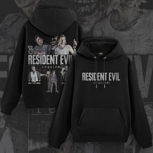 Może przedstawiać: Dwie czarne bluzy z kapturem. Jedna przedstawia grafikę postaci z gry "Resident Evil" i napis "RESIDENT EVIL requiem". Druga bluza ma tytuł gry w kolorze białym z przodu.