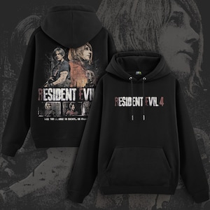Pode incluir: Hoodies pretos com gráficos de Resident Evil 4. Um hoodie apresenta o título do jogo em uma fonte desgastada, o outro exibe arte de personagens e o título. Ambos têm capuz com cordões e um bolso frontal.