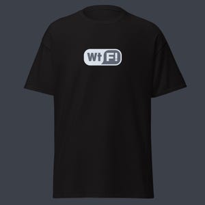 Puede incluir: Camiseta negra con un diseño gráfico blanco y gris que dice "Wt F!" en una burbuja de diálogo. La camiseta de manga corta está hecha de un material suave. El diseño está centrado en la parte delantera.