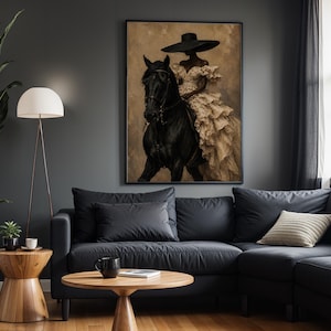 K&ouml;nnte beinhalten: Ein gerahmter Wandkunstdruck, der eine Figur mit einem breitkrempigen schwarzen Hut und einem volumin&ouml;sen, mehrlagigen cremefarbenen Kleid auf einem schwarzen Pferd zeigt. Das Bild hat einen strukturierten, neutralen Hintergrund und einen schwarzen Rahmen.