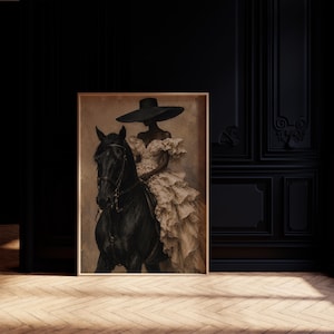 K&ouml;nnte beinhalten: Ein gerahmter Kunstdruck, der eine Person mit einem breitkrempigen schwarzen Hut und einem cremefarbenen R&uuml;schenkleid auf einem schwarzen Pferd zeigt. Das Kunstwerk hat einen ged&auml;mpften, strukturierten Hintergrund in Beige- und Braunt&ouml;nen.