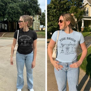 May include: Two t-shirts, one black and one light blue, with matching graphic designs. The black shirt reads "The Bach Club" with cocktail illustrations. The light blue shirt says "The Bride" with similar cocktail art. Both shirts are for a bachelorette party.