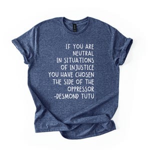 May include: A navy blue t-shirt with white text. The text reads: "IF YOU ARE NEUTRAL IN SITUATIONS OF INJUSTICE YOU HAVE CHOSEN THE SIDE OF THE OPPRESSOR -DESMOND TUTU."