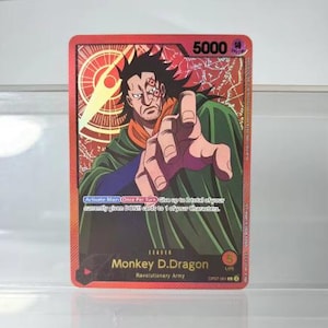 Può includere: Una carta collezionabile rossa con Monkey D. Dragon dell'Esercito Rivoluzionario. La carta presenta un ritratto del personaggio con un mantello verde e una sciarpa arancione. Il testo della carta include "Activate Main" e "5000".