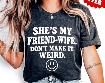 Op de afbeelding: Donkergrijs gemêleerd T-shirt met de tekst "SHE'S MY FRIEND-WIFE. DON'T MAKE IT WEIRD." en een smiley. Het shirt heeft ook de woorden "DARK GREY HEATHER" onderaan en een "SPECIAL OFFER" tag.