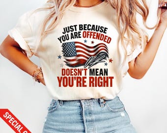 Op de afbeelding: Crèmekleurig T-shirt met de tekst "JUST BECAUSE YOU ARE OFFENDED DOESN'T MEAN YOU'RE RIGHT" in zwart en rood. Een Amerikaanse vlag met blauwe sterren en rode en witte strepen is afgebeeld.