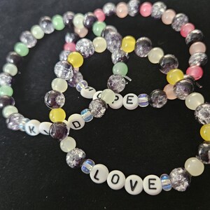 May include: Three beaded bracelets with a variety of colourful beads. One bracelet spells out "LOVE" with white letter beads. Another spells "HOPE". The bracelets feature green, yellow, pink, and purple beads.
