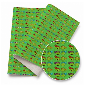 May include: A sheet of green faux leather fabric featuring a repeating pattern of cartoon turtle faces wearing masks in red, blue, purple, and orange. The material has a textured surface and a light-colored, fuzzy backing visible at the corner.