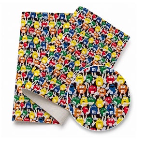 May include: A rectangular sheet of faux leather fabric featuring a repeating pattern of colorful M&M characters in red, yellow, green, blue, and orange on a black background, with a circular inset showing a magnified view of the same print.
