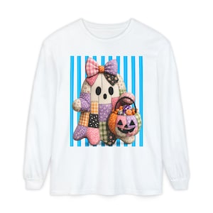 May include: A white long-sleeve shirt featuring a central graphic of a patchwork ghost figure with a large bow on its head, holding a pumpkin-shaped basket filled with colorful candies, set against a background of vertical blue and white stripes.