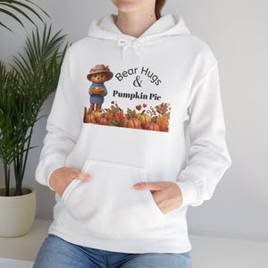 May include: A white hooded sweatshirt featuring a graphic of a teddy bear in a hat and blue sweater holding a pumpkin pie. The text reads Bear Hugs & Pumpkin Pie above an illustration of autumn leaves, small pumpkins, and red hearts.