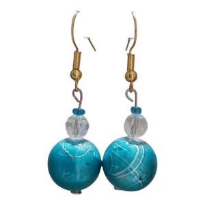 May include: A pair of dangle earrings with gold-colored hooks and accents. Each earring features a clear, faceted bead above a large, turquoise-colored, marbled bead. White lines swirl across the turquoise beads.
