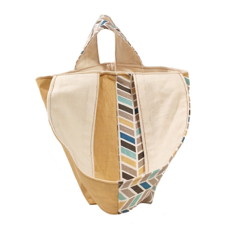 May include: A beige and yellow fabric tote bag with a geometric pattern in shades of blue, gray, and yellow. The bag has a single handle and a wide opening.