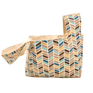 May include: A beige fabric tote bag with a chevron pattern in shades of brown, blue, and yellow. The bag has a single handle and a wide opening.